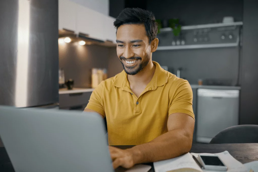 A smiling man using a laptop in his kitchen.