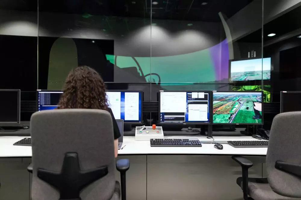 Engineer at work, operating multiple computer monitors in a control room with a large screen display.