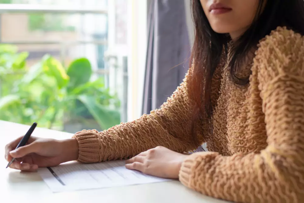 Woman signing document at a bright desk with greenery outside the window