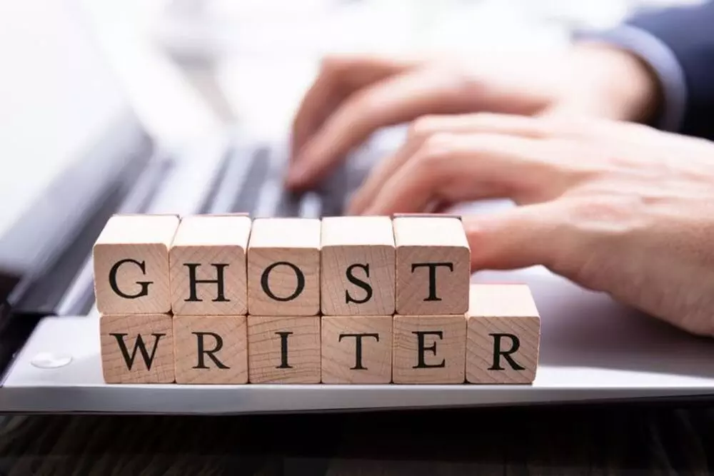 Hands typing on a laptop keyboard with wooden blocks spelling out Ghost Writer.