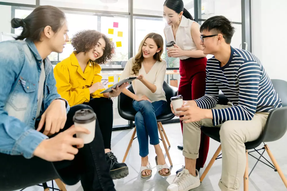 Group of young professionals collaborating in a modern office setting, holding coffee cups and tablets